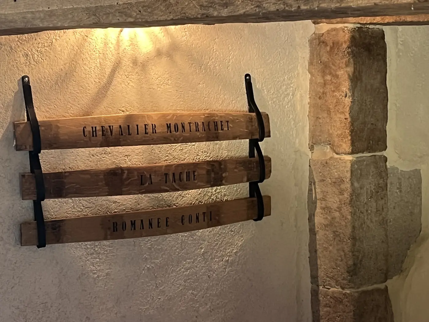 Trois douelles peintes Chevalier-Montrachet, La Tâche et Romanée-Conti mises en lumière dans une cave voûtée