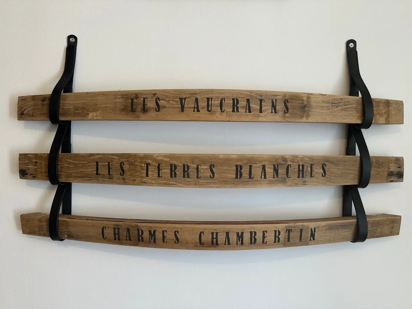 Trois douelles de tonneau peintes Les Vaucrains, Les Terres Blanches et Charmes-Chambertin fixées au mur par des attaches en cuir noir
